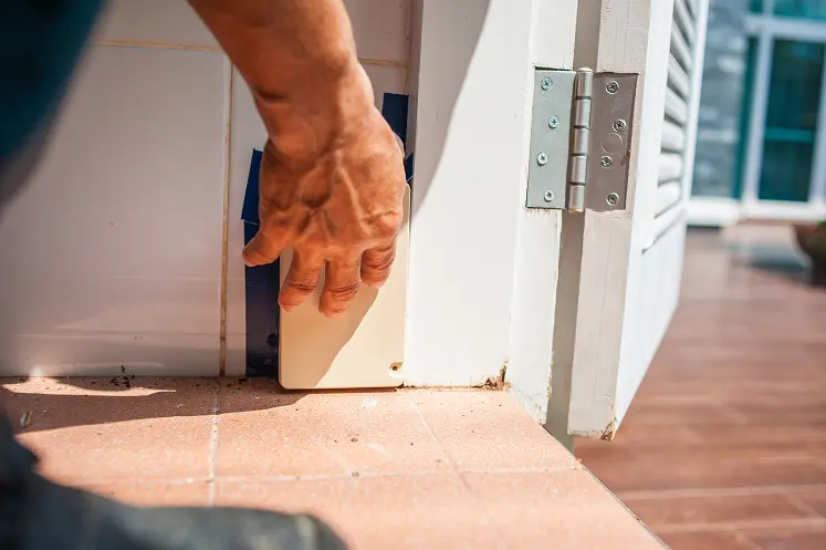 An SOS Exterminating pest technician places a termite trap at the base of a door frame